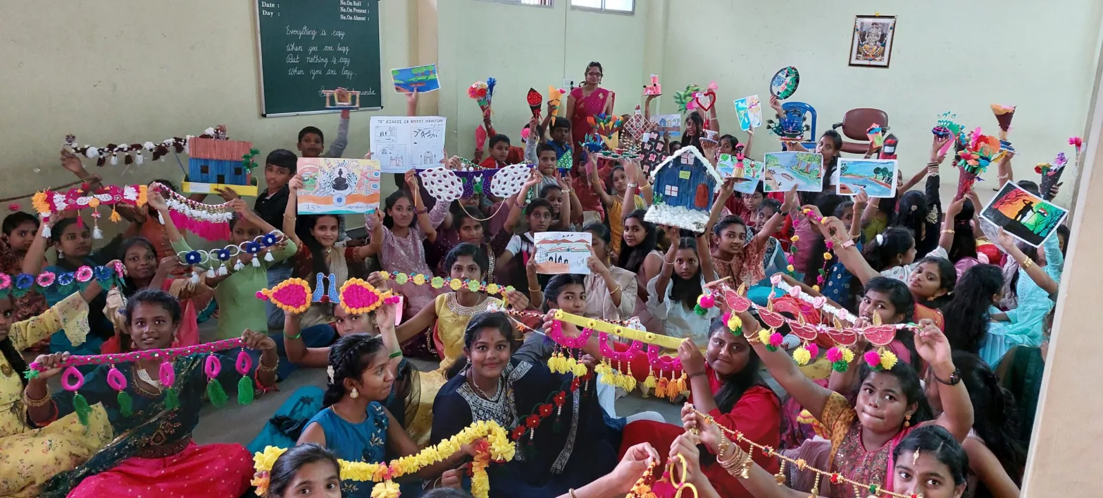 Students holding up handmade crafts and drawings in a decorated classroom