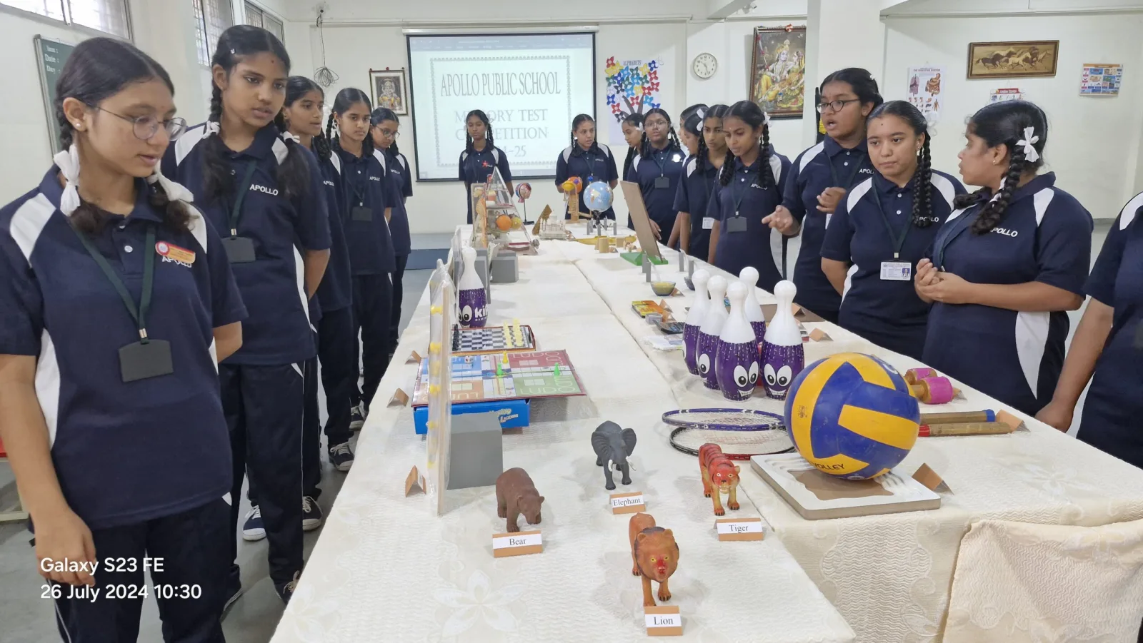 Students standing around a long table of objects during a memory test competition