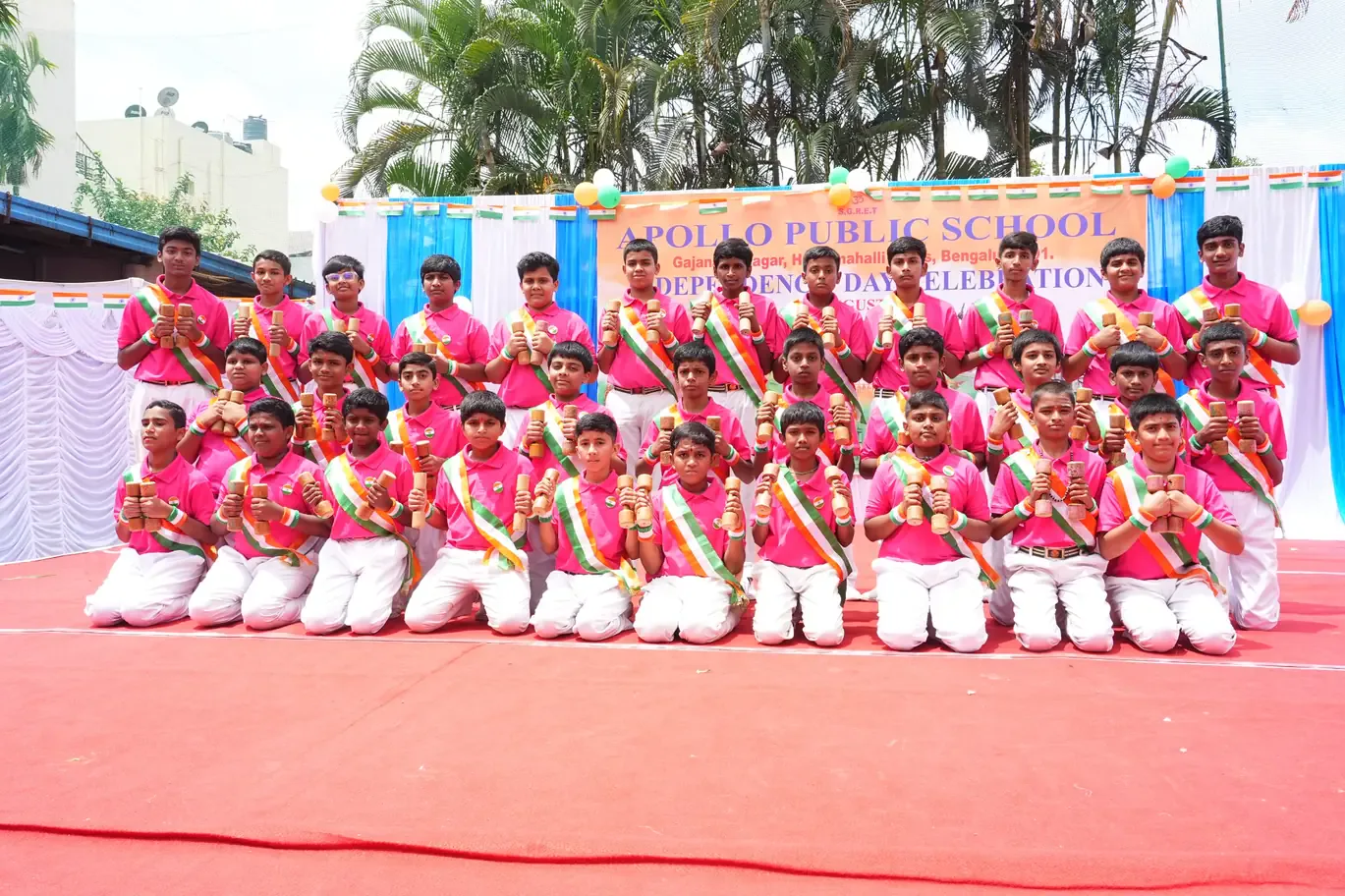 A group of students in pink and white costume performing a dance on an outdoor stage