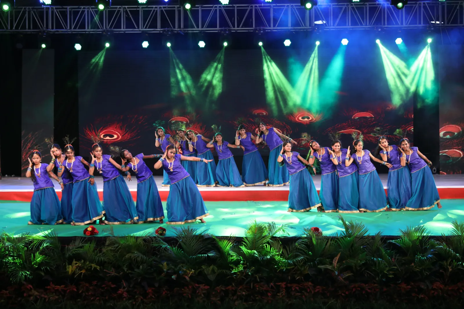 Students in blue and purple costume performing a dance in front of a peacock-themed backdrop