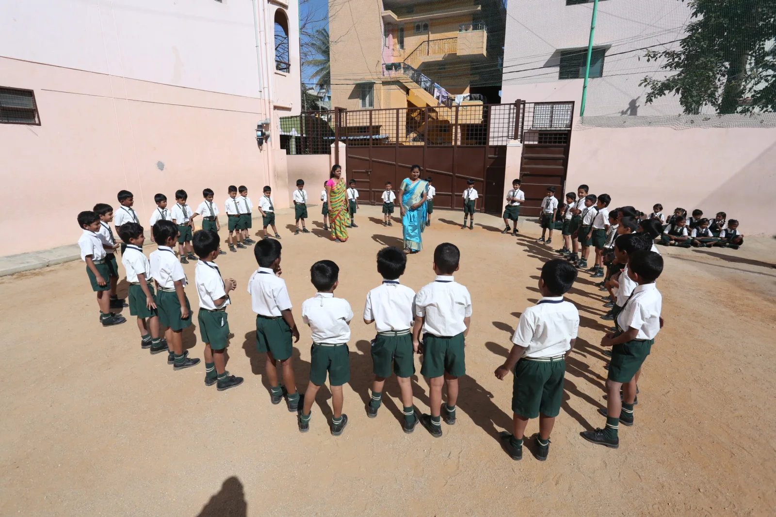 Young students standing in a circle formation with a teacher on the school ground