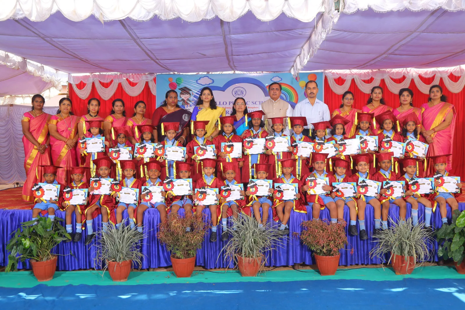 UKG children holding certificates together on a decorated graduation stage