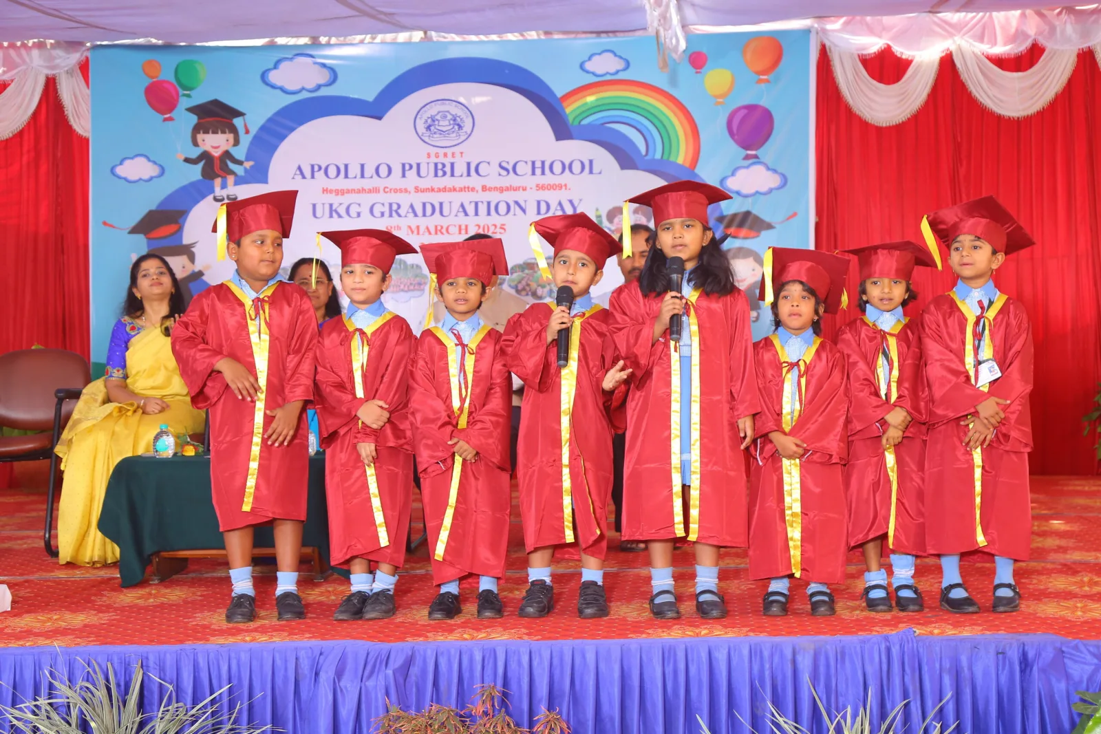 UKG children in graduation gowns and caps standing together on stage